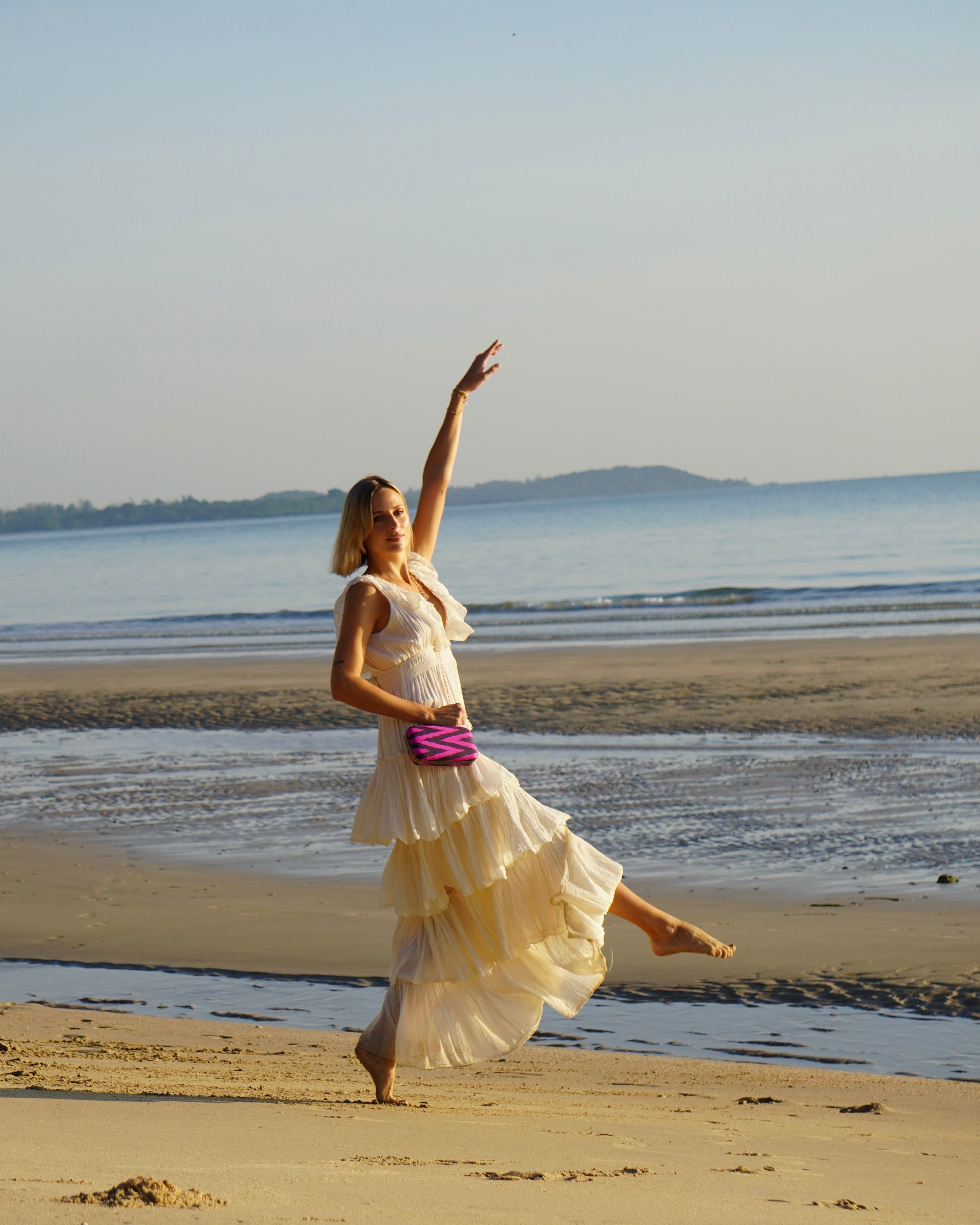 Woman in a white dress dancing on a beach with a pink silk ikat handwoven clutch handbag