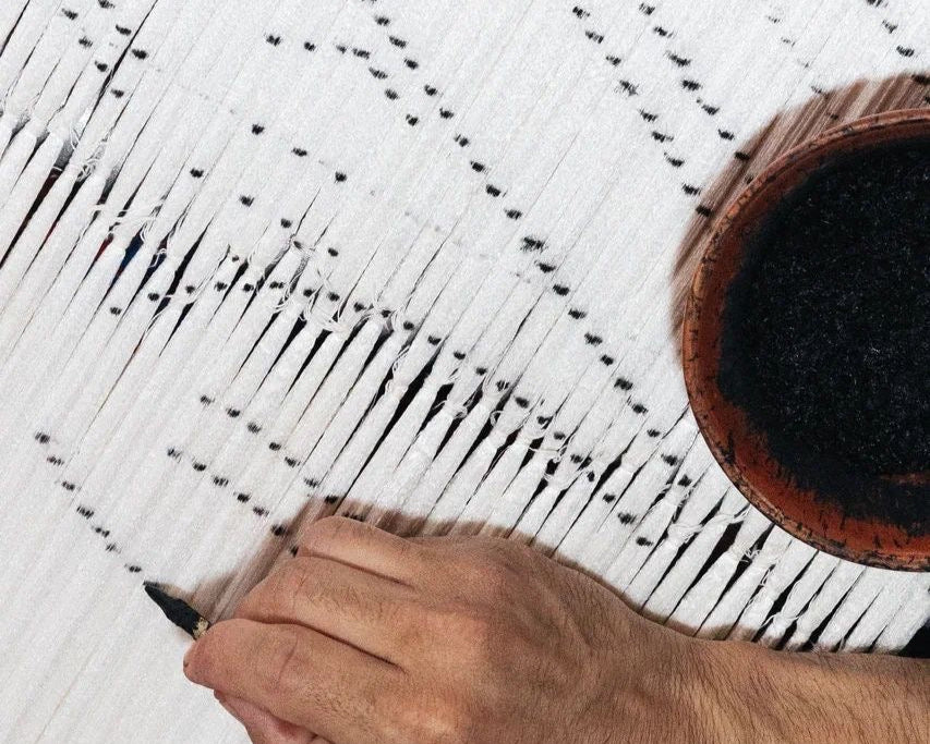 Hand weaving a pattern on a white fabric with a wooden tool.