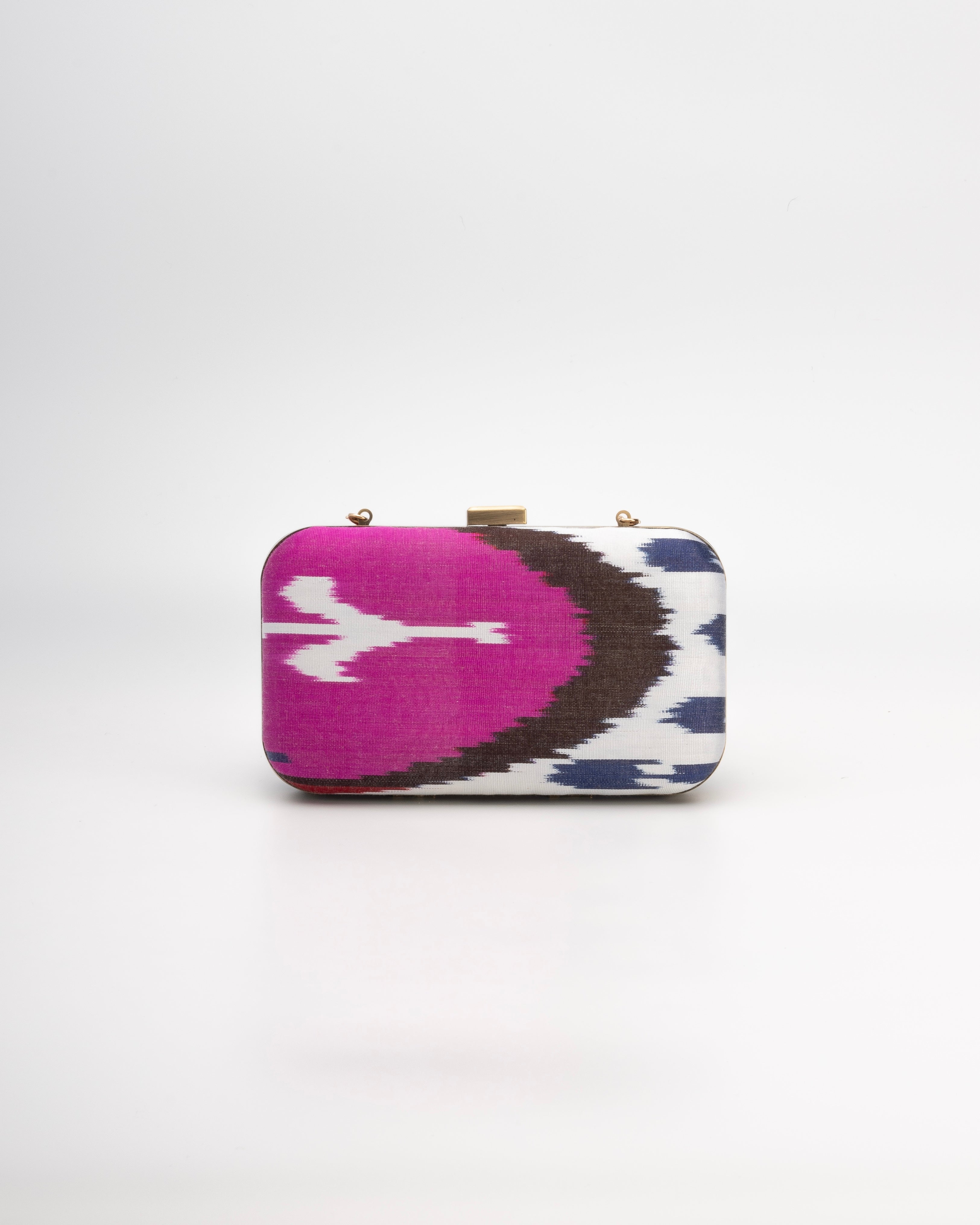 A striking silk handwoven Ikat clutch by Frankitas, featuring a vibrant mix of pink, white, blue, and black.