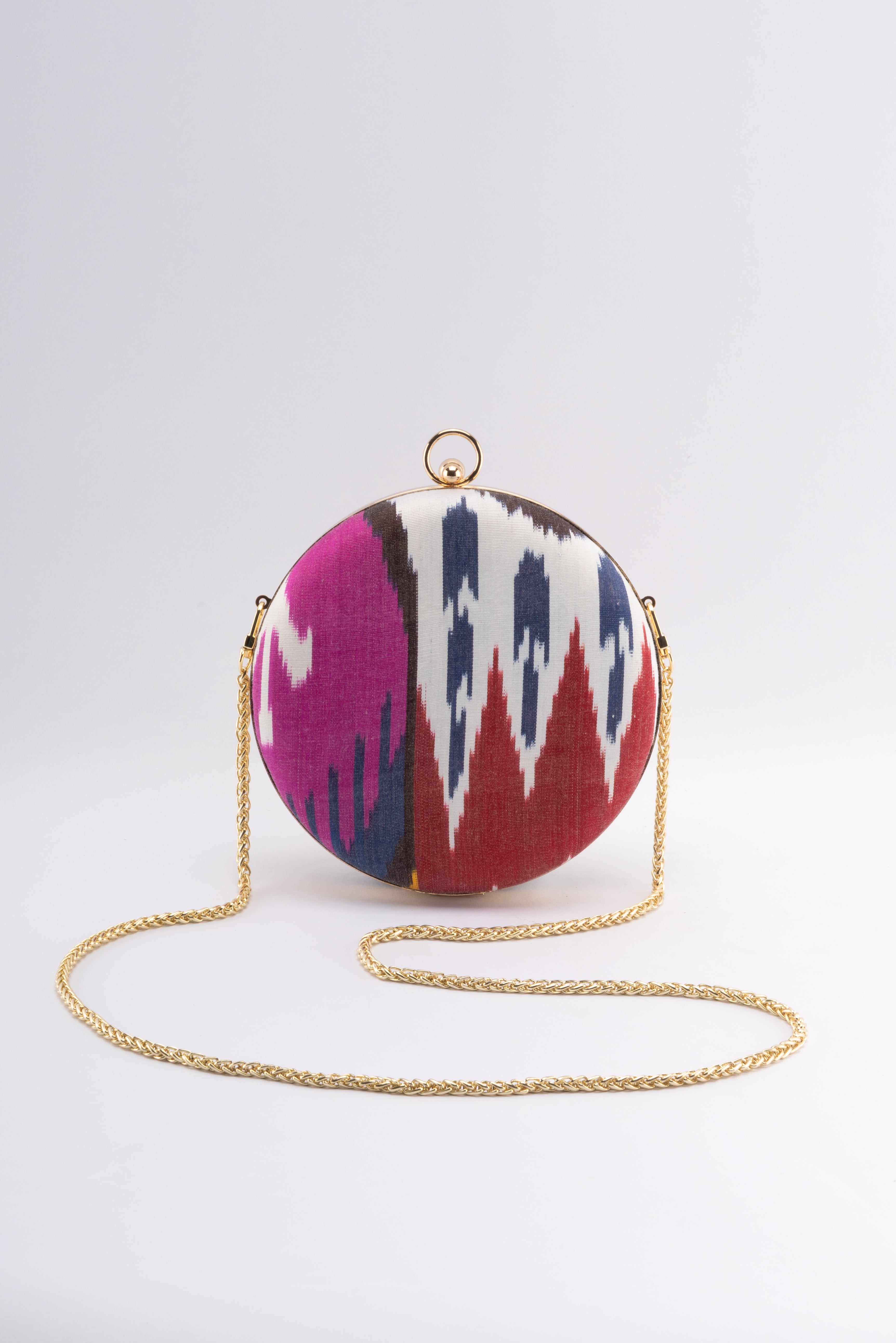 The signature Puteri Round clutch by Frankitas displays an intricate and colorful handwoven silk ikat design with a gold crossbody strap