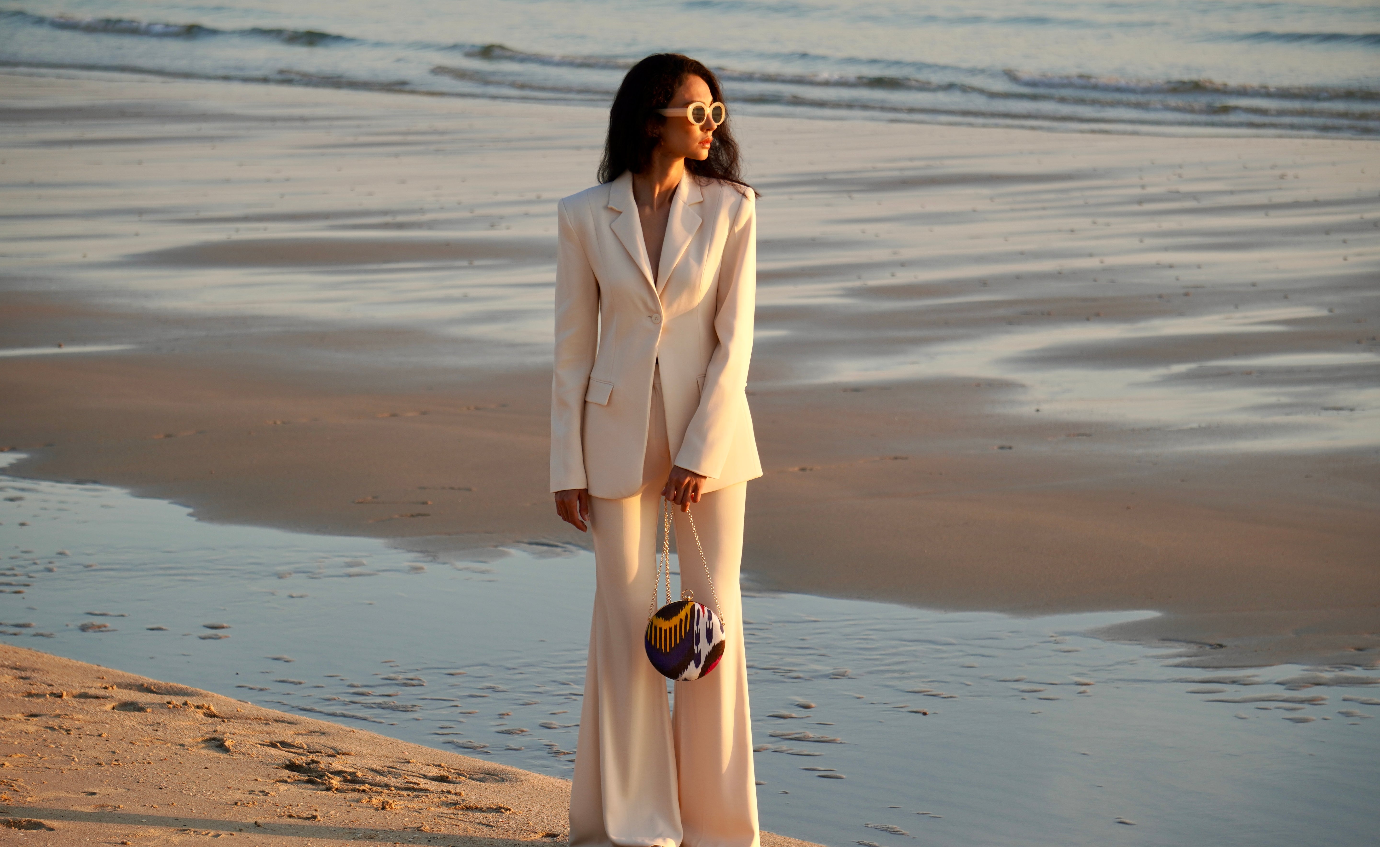 Woman in a white suit standing on a beach holding a contemporary multicolor Frankitas silk ikat handwoven artisan clutch bag 