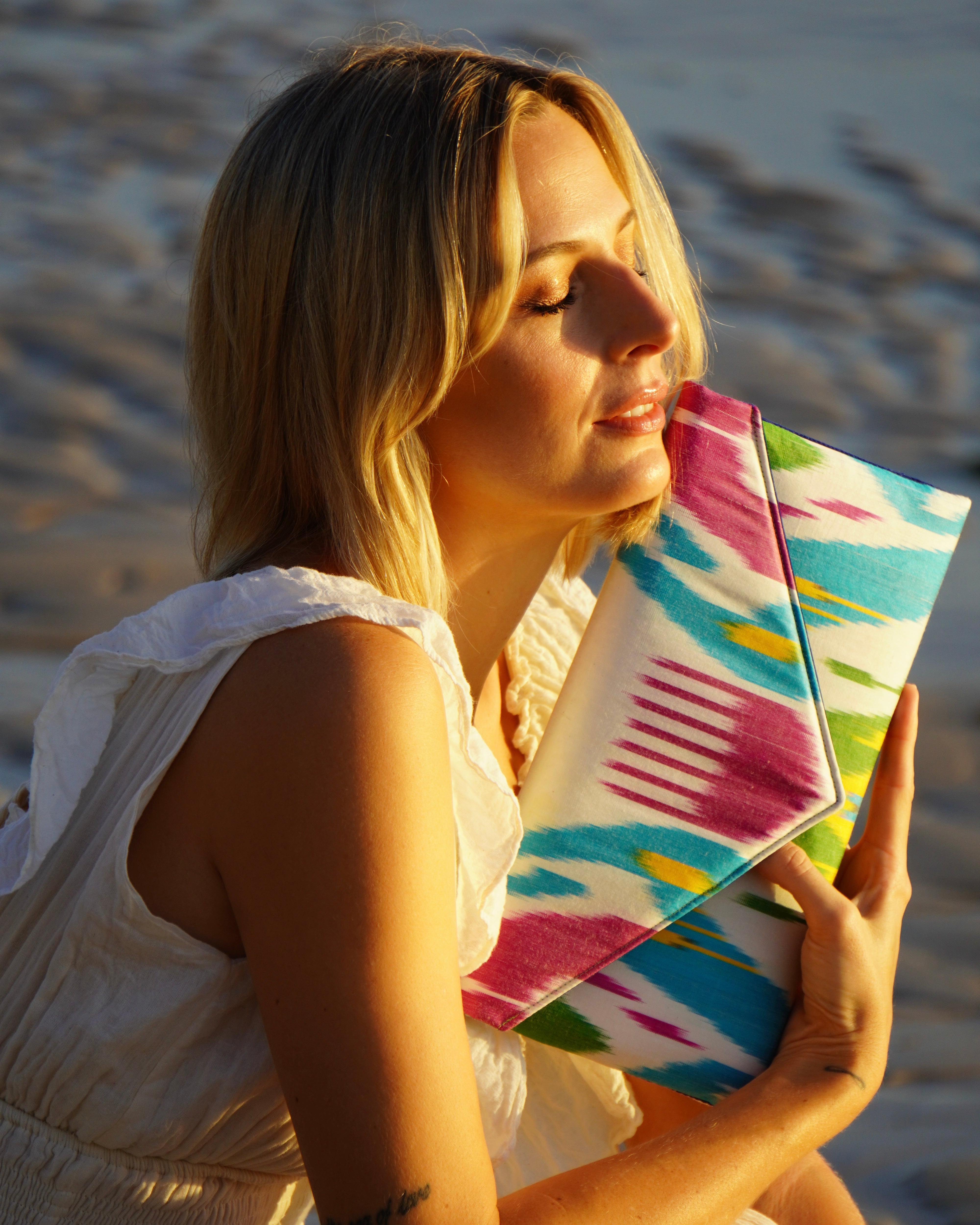 Woman holding a colorful Frankitas silk ikat artisan clutch handbag on a beach