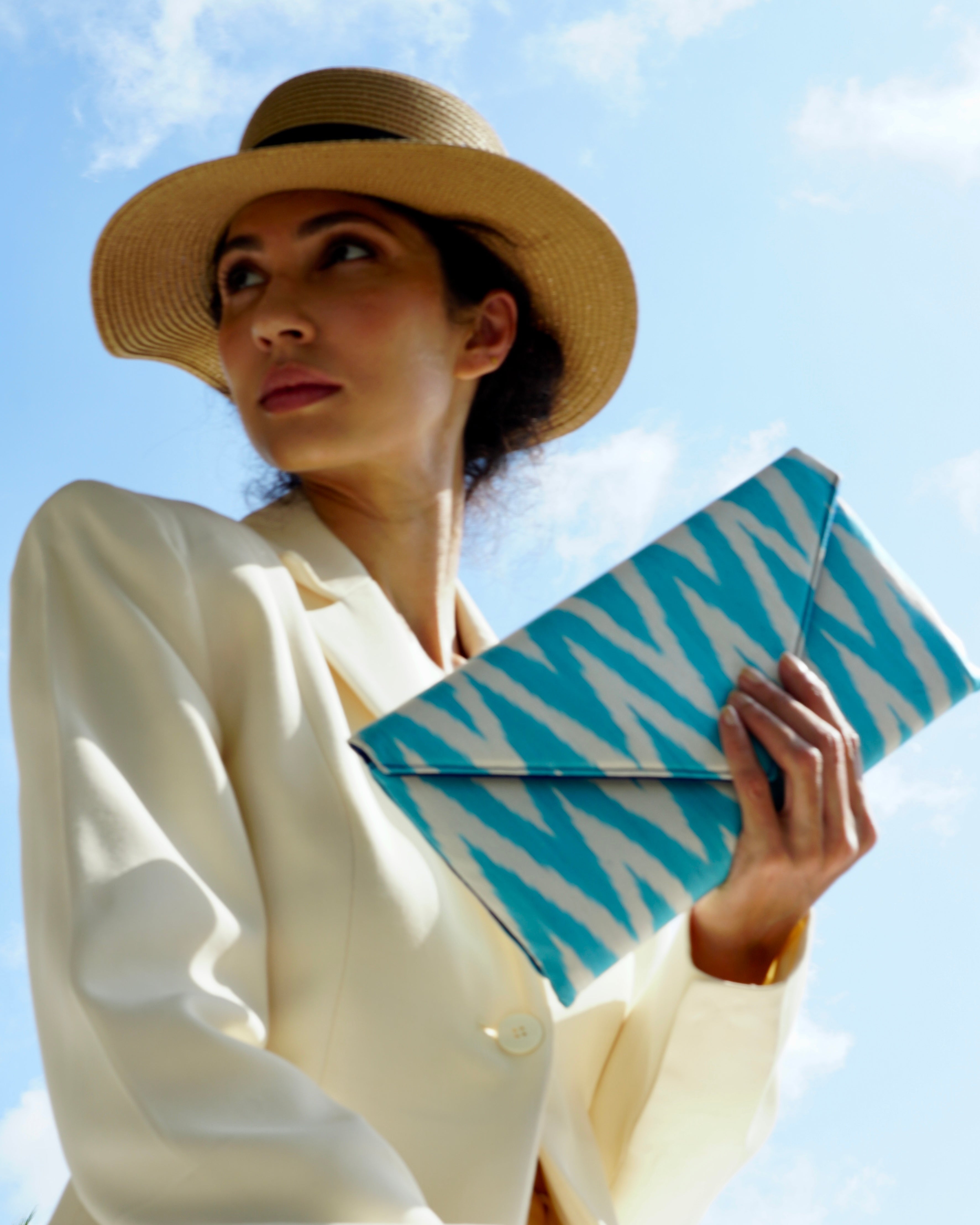 Woman holding a blue and white patterned silk ikat handwoven artisan clutch against a clear sky